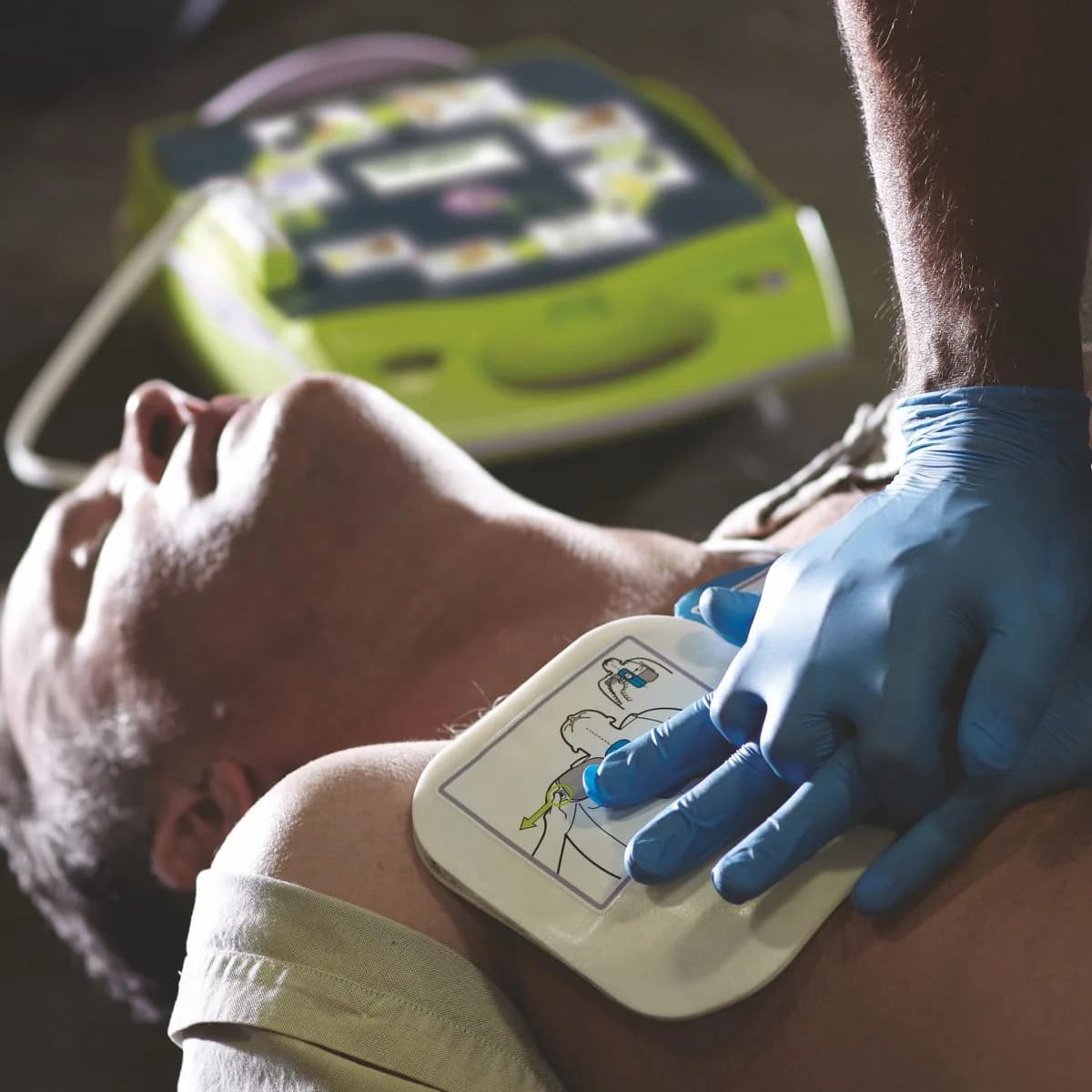 Dłonie uciskające klatkę piersiową przez czujnik elektrody CPR-D-padz, obok ZOLL AED Plus