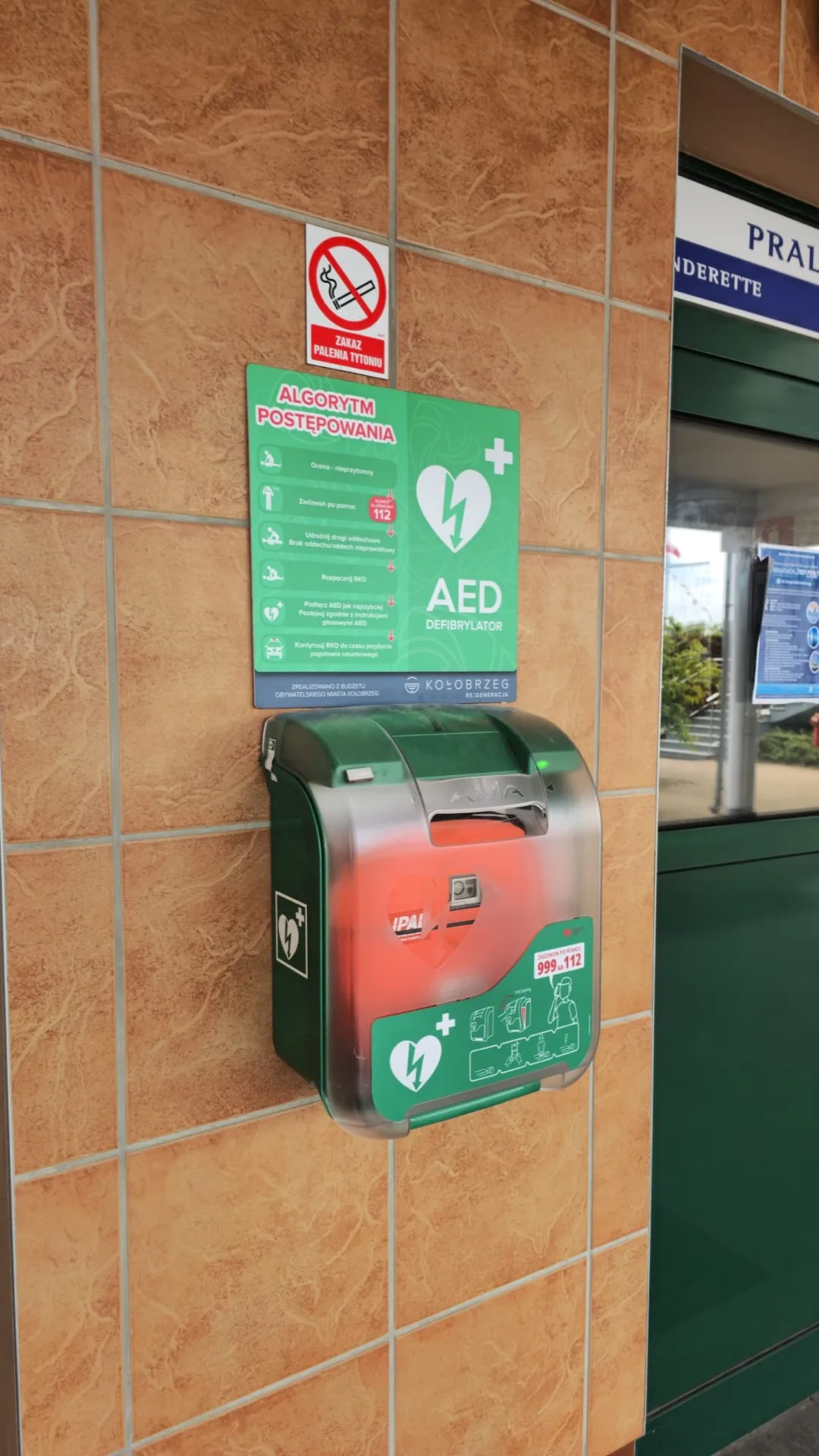 Zewnętrzna szafka AED z oznakowaniem na ścianie budynku w Kołobrzegu