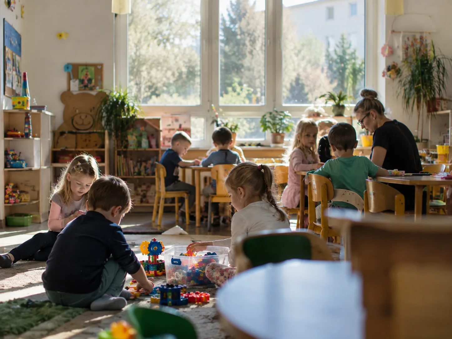 Dzieci bawiące się na dywanie w sali przedszkolnej pod opieką wychowawczyni