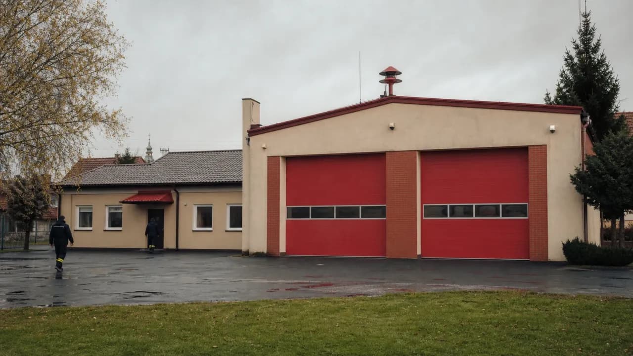 Budynek remizy OSP z dwiema czerwonymi bramami garażowymi